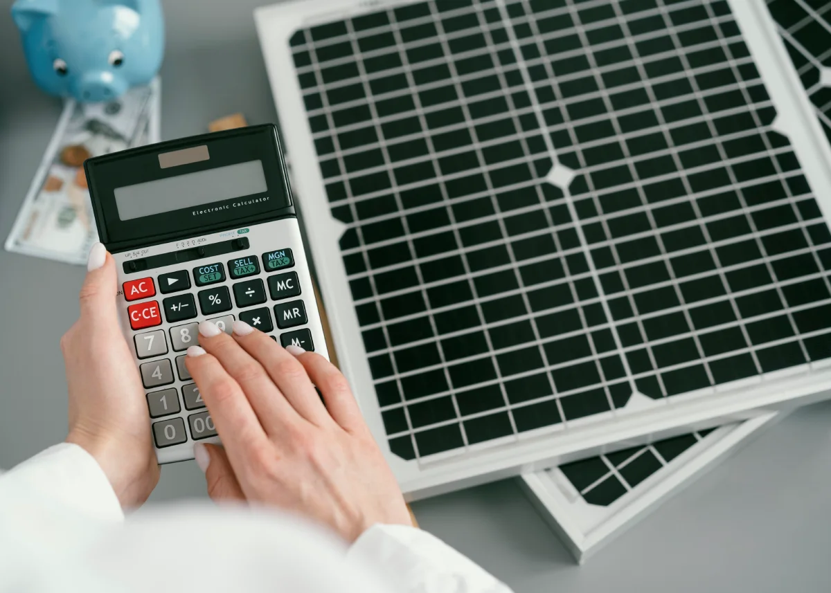 Person calculating costs beside solar panels and savings jar